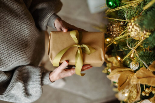 Top View Of Mature Female Hands Holding Christmas Gift With Golden Ribbon. Gift Wrapped Box